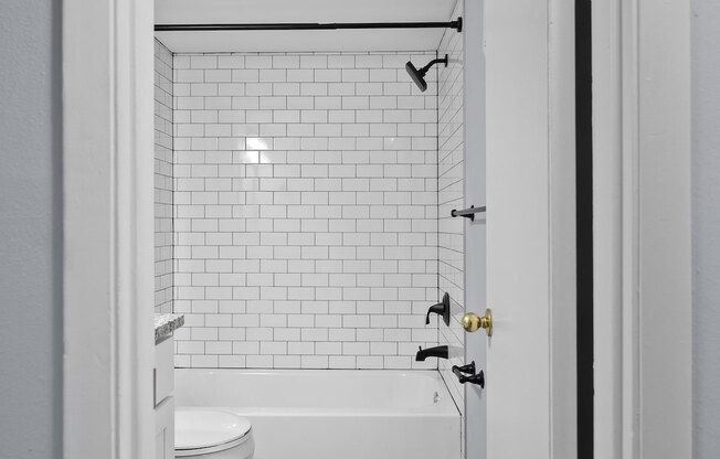 a bathroom with white subway tile and a tub and a toilet