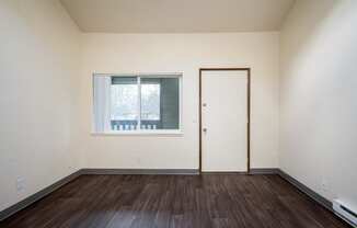 the bedroom of an empty apartment with wood flooring and a window