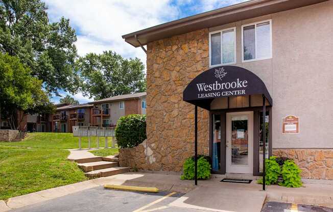 The front of the Westbrooke Leasing Center is shown with a stone facade and a green lawn.