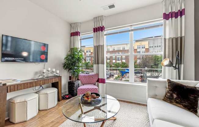 A living room with a white couch, a glass coffee table, and a flat-screen TV mounted on the wall.