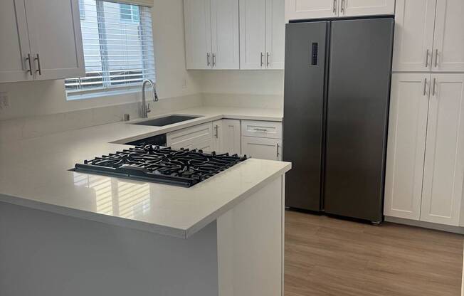 A kitchen with wood flooring, white cabinets and a black fridge.