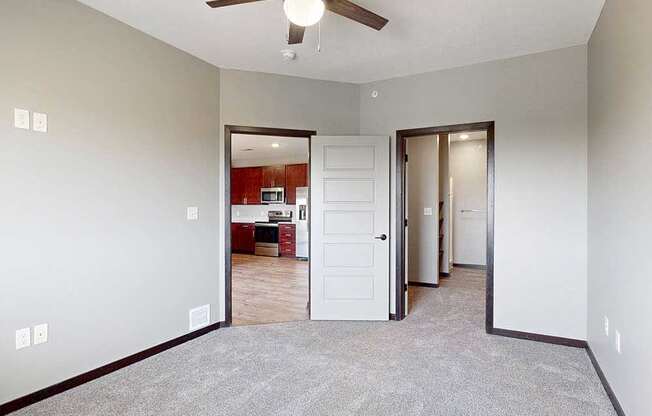 A carpeted bedroom with a ceiling fan and a walk-in closet and attached bathroom.