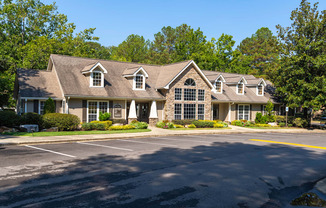 A large house with a grey roof and white trim is surrounded by trees.