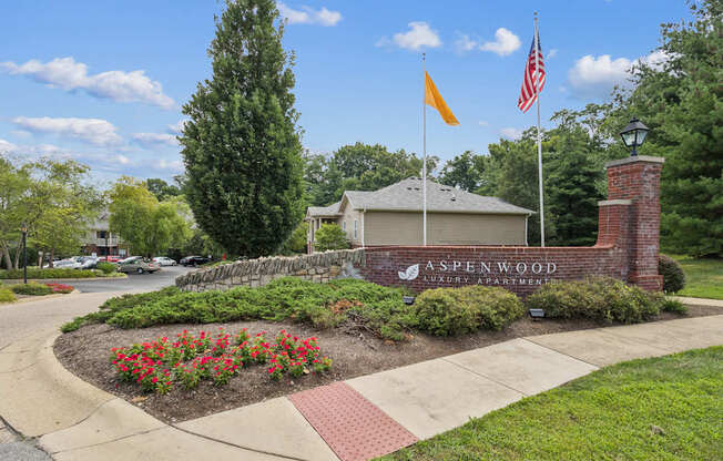 The image shows a well-maintained entrance to A Spenwood Apartments with a flagpole and a brick wall.