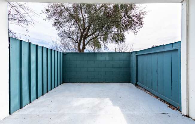 a garage with a blue fence and a tree behind it at Avenue Two Apartments, Redwood City  , CA 94063