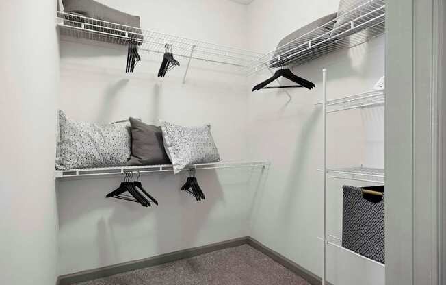 A small closet with a hanging rod and a shelf with pillows and a pair of gloves.