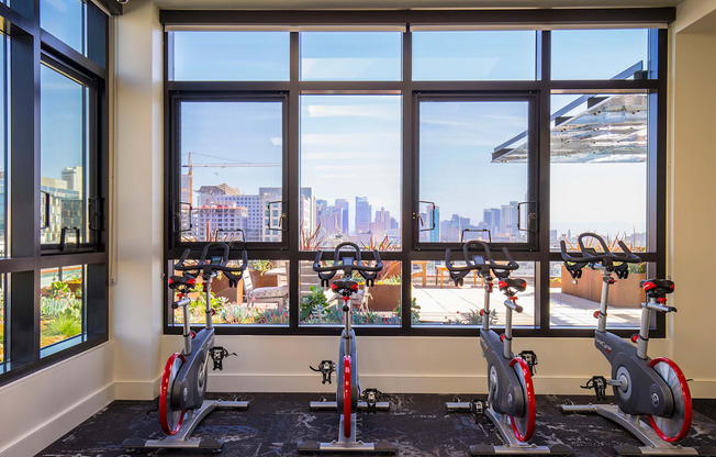 A gym with exercise bikes and a view of the city outside the window.