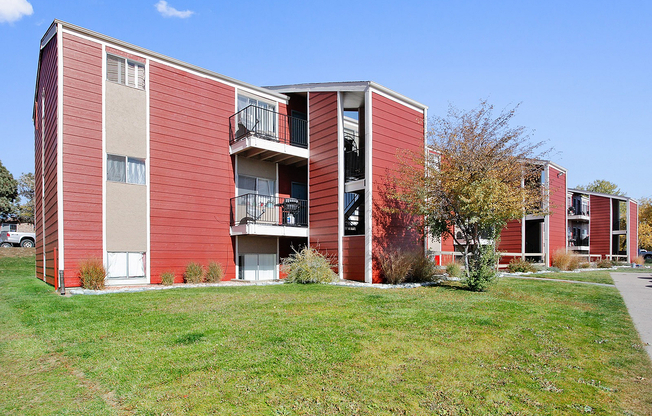 Charming red apartment complex with private balconies, nestled in a lush green landscape, perfect for modern living.