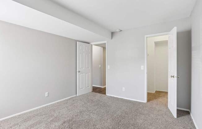 A room with white walls and carpeted floor with a door on the right.