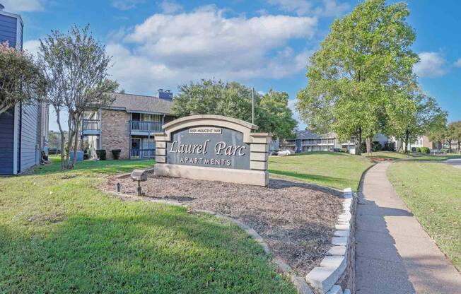 The entrance sign to Laurel Park Apartments is surrounded by a well-maintained lawn and trees at Laurel Parc apartments in Shreveport, LA.