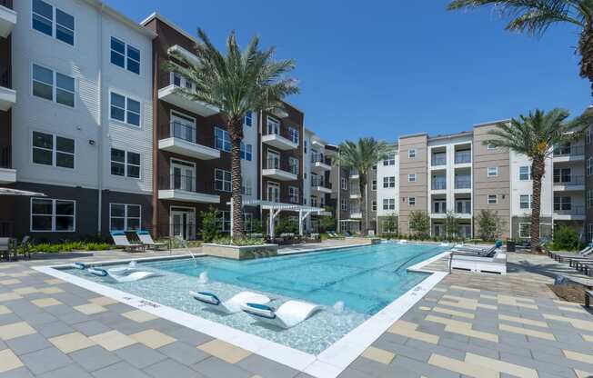 a swimming pool in front of an apartment building with palm trees