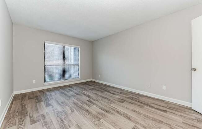 A room with wooden flooring and a window with blinds.