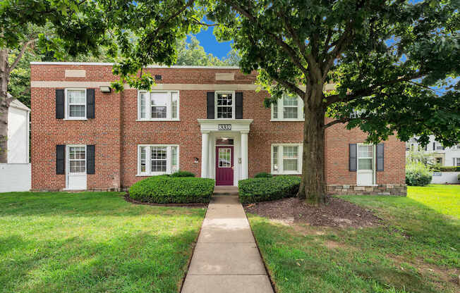 A red brick house with a tree in front.