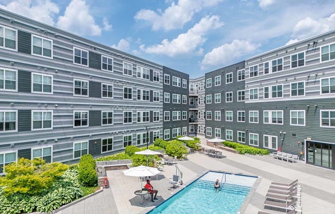 A large swimming pool surrounded by lounge chairs and umbrellas in the middle of a courtyard.