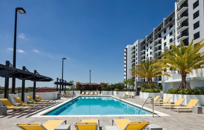 The pool area at our apartments in Miami, featuring yellow reclining chairs, a shade structure, and a sparkling blue pool.