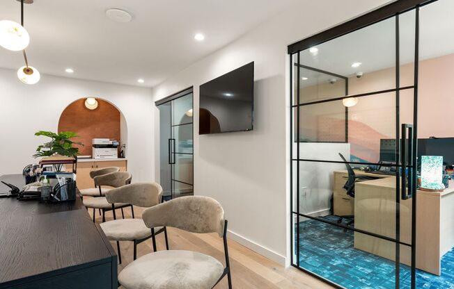 A modern office space with a wooden desk, chairs, and a television mounted on the wall.
