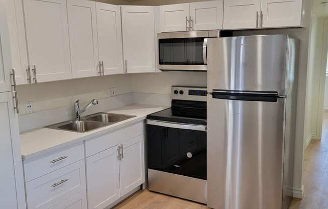 Well lit kitchen with white cabinets and new appliances and hallway to bathroom and bedroom at the Atrium Apartments in San Diego, CA.