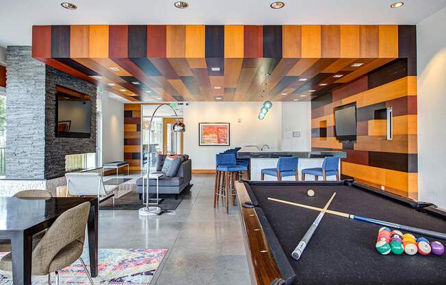 A billiard table is in the middle of a room with a TV, chairs, and a fireplace.