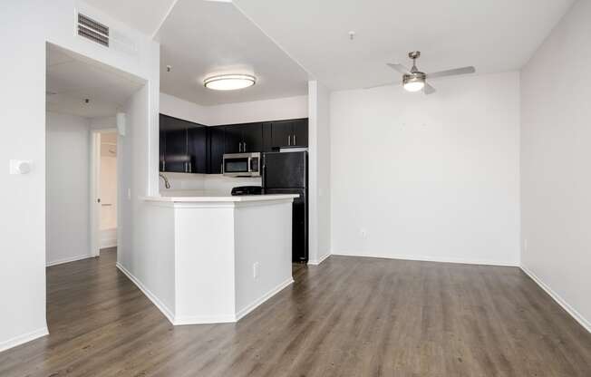 a living room with white walls and a kitchen with black cabinets