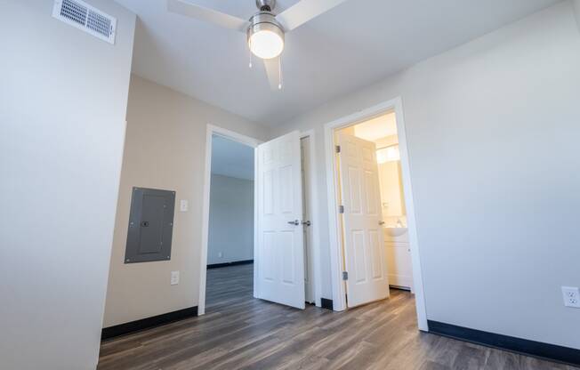 a living room with white walls and wood floors and a door to a bathroom