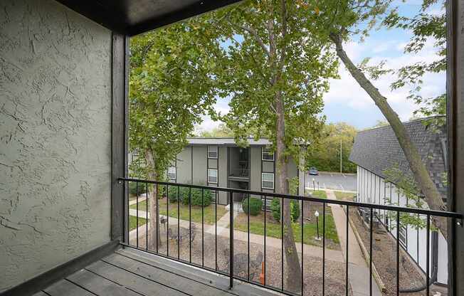 A balcony with a black railing and a view of a tree and a building.
