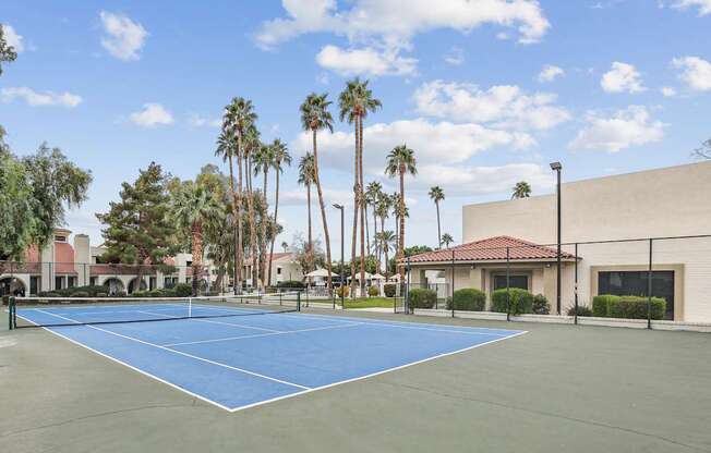 A tennis court surrounded by palm trees and a building.