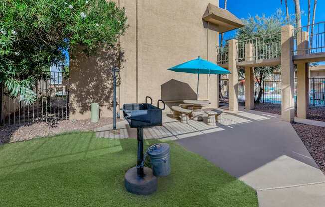 A patio with a blue umbrella and a grill.