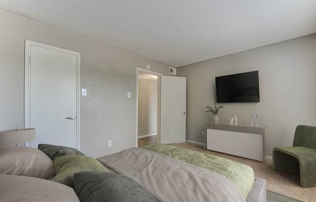 A bedroom with a bed, a chair, and a TV on the wall.