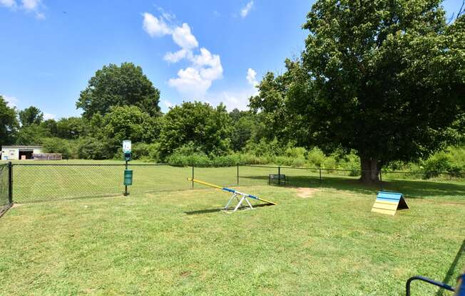 a seesaw sits in the middle of a grassy area with trees in the background