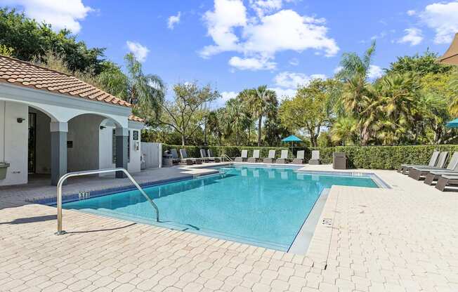 A swimming pool surrounded by a tiled patio and a white building with a red roof.