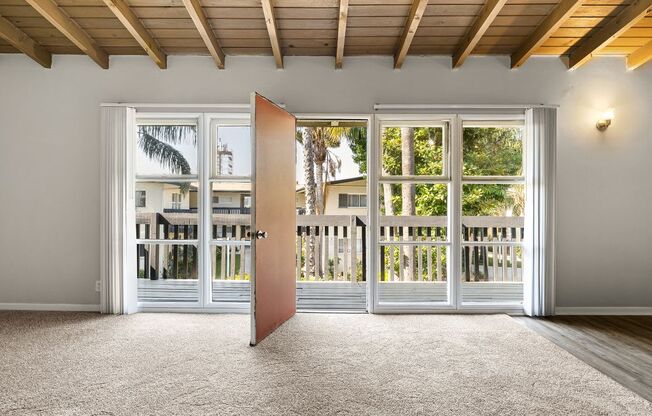 A room with a carpeted floor and a wooden ceiling with a door open to a balcony.