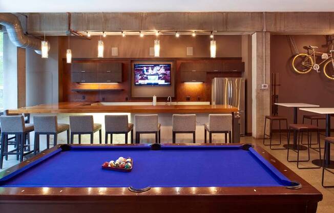 A pool table with a blue cloth and a television mounted on the wall.