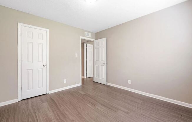 an empty living room with white doors and wood flooring