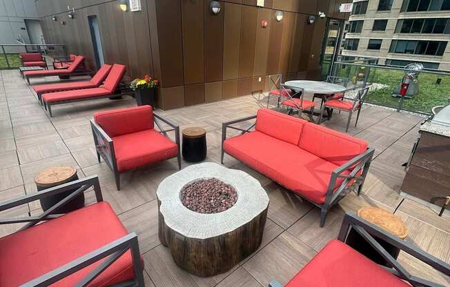 A wooden table with a fire pit in the middle of a patio with red couches.