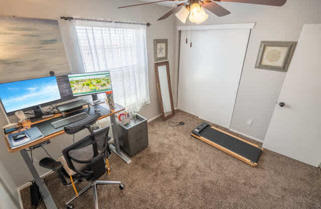A room with a desk, chair, and a treadmill.