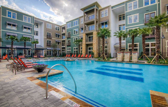 an outdoor pool with lounge chairs and a firepit in front of an apartment building