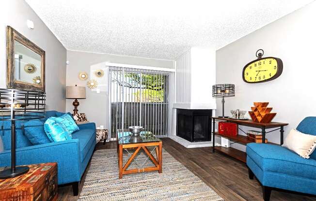 A living room with a blue couch, a wooden coffee table, and a large clock on the wall.
