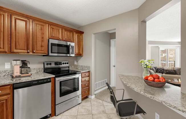 A kitchen with a black fridge and stove, a microwave above it, and a black chair in front of the counter.
