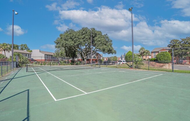 A tennis court surrounded by a fence and trees at Magnolia apartments in Shreveport, LA