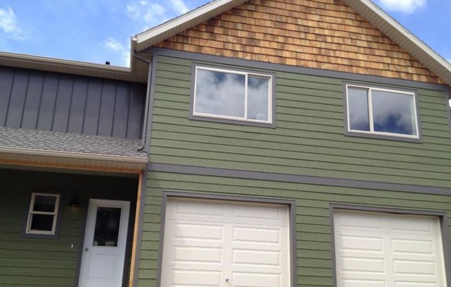 a green house with two white garage doors at Copper Pines, Bozeman