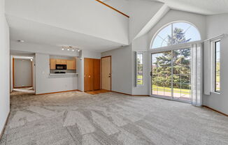 an empty living room with a large window and a door to a kitchen