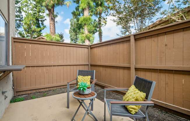a patio with two chairs and a table in front of a fence
