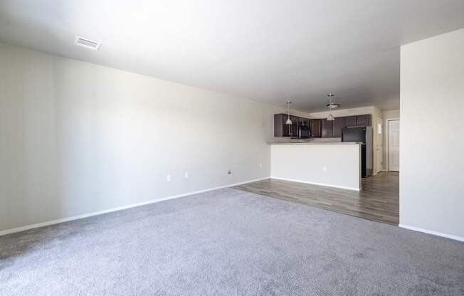 A spacious living room with a grey carpet and white walls.