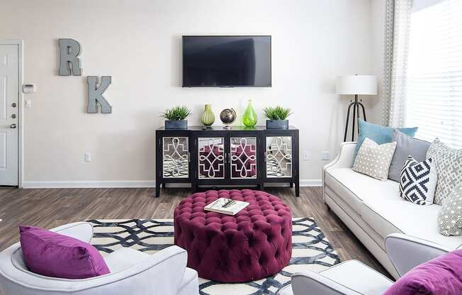 A living room with a white couch, a red ottoman, and a TV mounted on the wall.