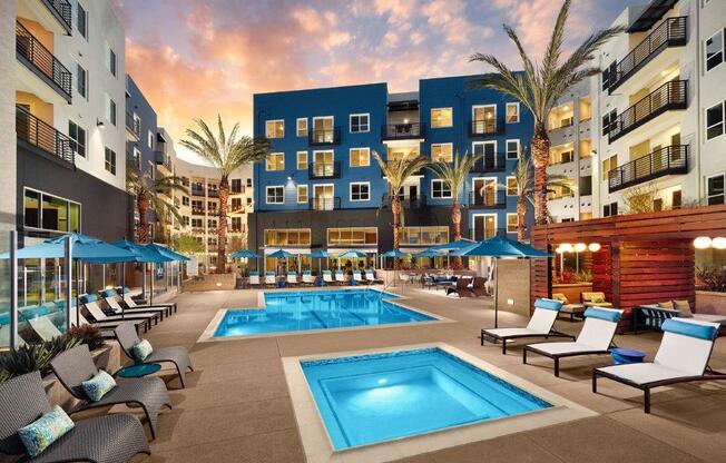 a pool with chairs and umbrellas in front of an apartment building