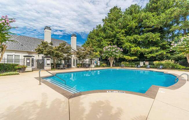 A large outdoor swimming pool surrounded by a fence and trees.