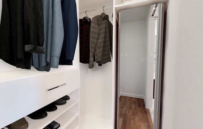 a walk in closet with a mirror and some clothes hanging on the wall