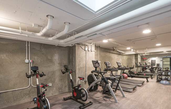 a row of exercise bikes in a room with concrete walls and a skylight