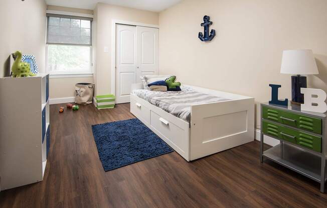 A bedroom with a white bed, a blue rug, and a green drawer.