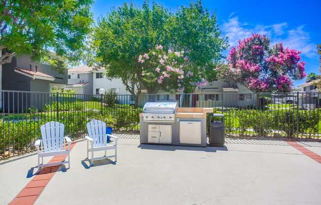 a patio with two chairs and a grill in front of some trees